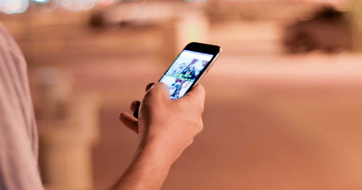 A person holds a smartphone displaying a social media feed, unaware of the AI systems embedded in the apps they use every day.